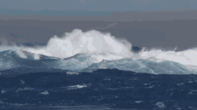 a large wave in the ocean with a mountain in the background