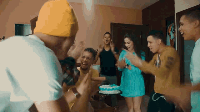 a group of young people are dancing around a birthday cake