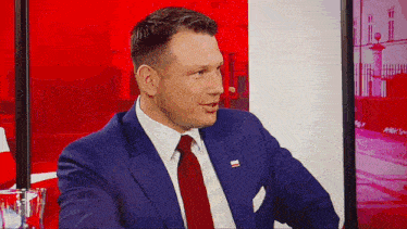 a man in a blue suit and red tie is sitting in front of a screen