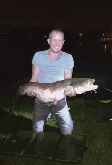 a man kneeling down holding a large fish