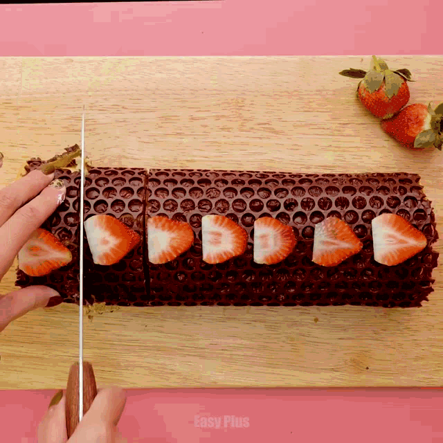 a person is cutting a chocolate cake with strawberries on it that says easy plus on the bottom