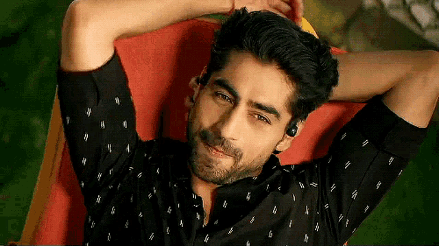 a man in a black shirt is laying down with his hands behind his head and a smile on his face