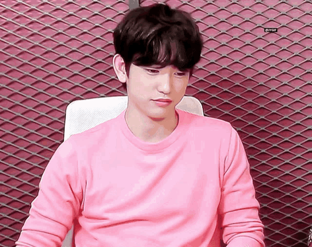 a young man in a pink shirt is sitting in front of a metal fence