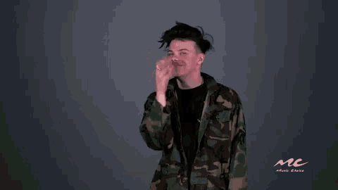 a young man in a camo jacket is making a funny face .