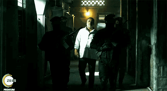 a man in a white shirt is being escorted by a group of soldiers with a zees premium logo on the bottom right