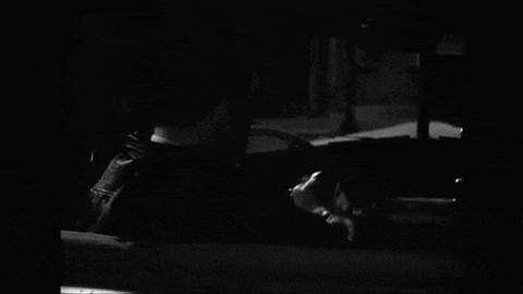 a black and white photo of a man in a suit smoking a cigarette in a dark room .