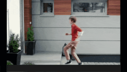 a boy in a red shirt is running on a sidewalk in front of a building
