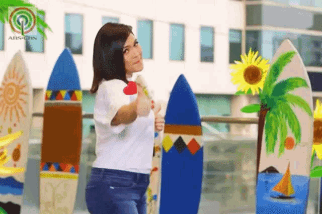 a woman is holding a surfboard in front of a building that says abs-cbn on it