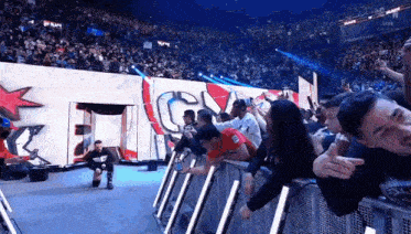 a man in a red shirt is kneeling down in front of a crowd at a wrestling match .