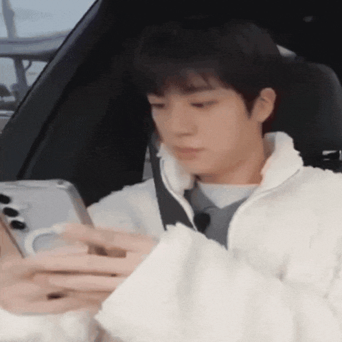 a young man is sitting in the back seat of a car looking at his cell phone .