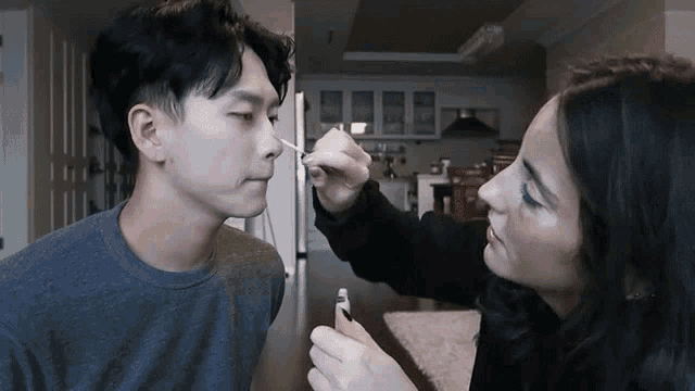 a woman is cleaning a man 's nose with a swab