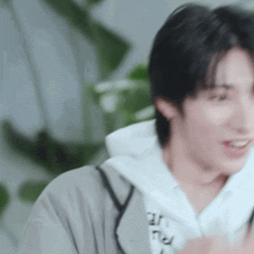 a young man wearing a hoodie and a white shirt is smiling while holding a cell phone .