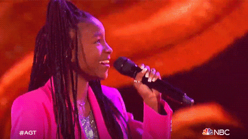a man and a woman are singing on a stage with a nbc logo in the background .