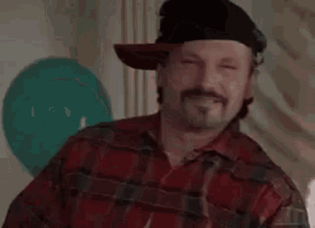 a man with a beard wearing a hat and a plaid shirt is saying wazzup .