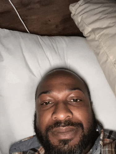 a man with a beard is laying on a bed with a white pillow
