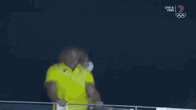 a man in a yellow shirt and a woman in a white mask are standing next to each other on a railing .
