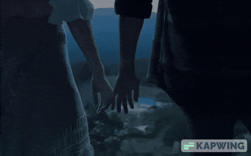 a couple holding hands in a dark room with the caption kapwing