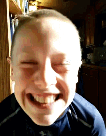 a young boy with a shaved head is smiling with his eyes closed