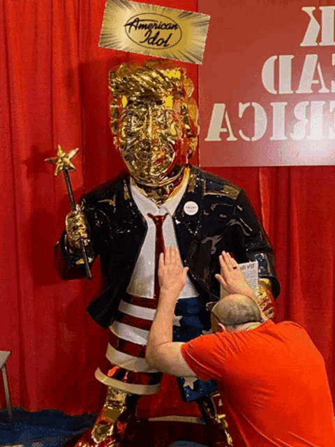 a man is touching a trump statue with an american idol balloon