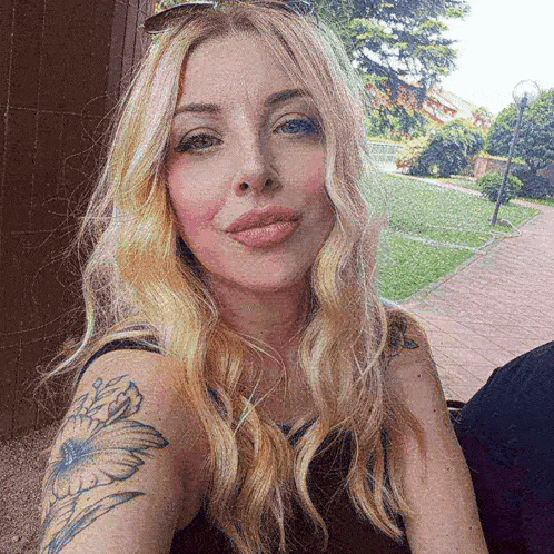 a woman with blonde hair and a tattoo on her arm is taking a selfie