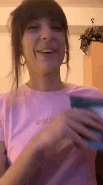 a woman in a pink shirt is smiling while holding a cell phone