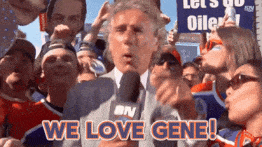 a man holding a microphone in front of a crowd says we love gene