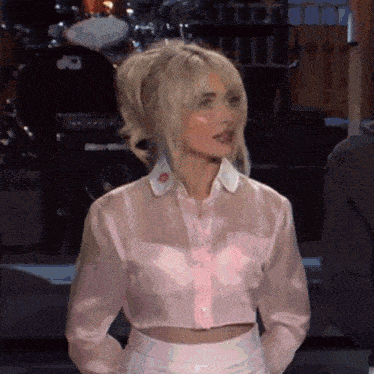 a woman is wearing a pink crop top and white skirt .