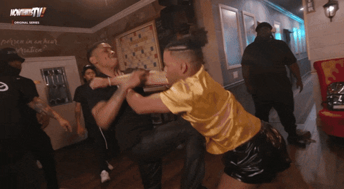 a man in a yellow shirt is fighting another man in a black shirt in front of a sign that says now that tv