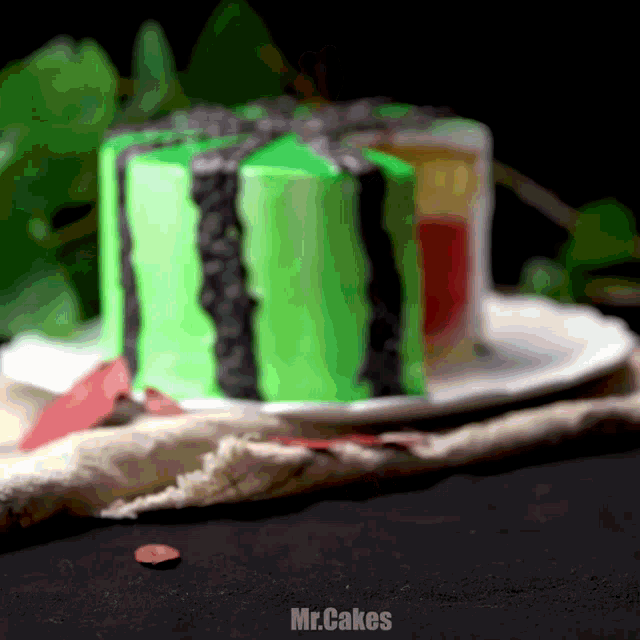 a watermelon shaped cake on a white plate with mr.cakes written on the bottom right