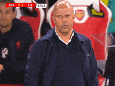 a man stands in front of a scoreboard that says ars 2-1 liv 67 38