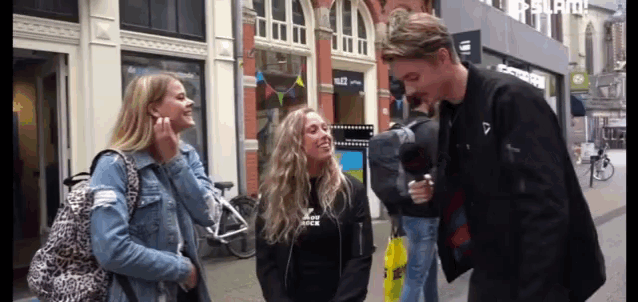 a man in a black jacket is talking to two women on a sidewalk