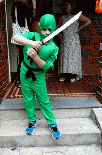 a young boy in a green ninja costume is holding a large sword