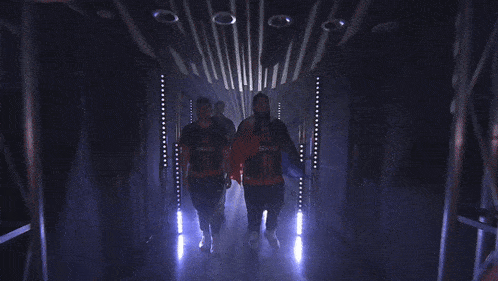 a group of people are walking through a dark hallway with purple lights