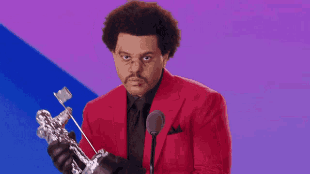 a man in a red suit is holding a trophy in front of a microphone and making a funny face .