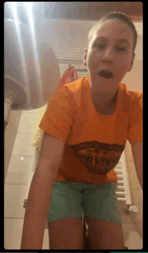 a girl wearing an orange shirt that says calvin klein is standing in a bathroom