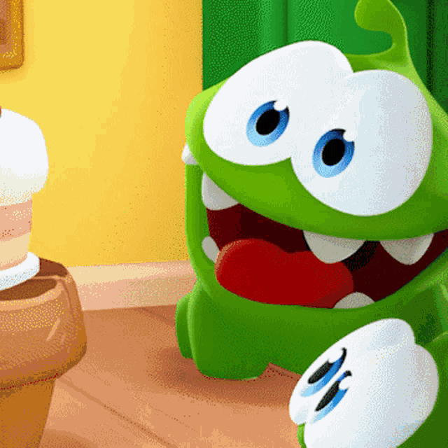a green cartoon character with a red tongue standing next to a cupcake