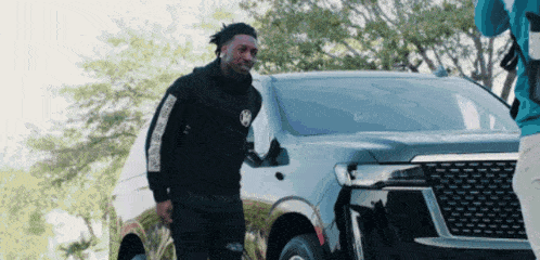 a man in a black hoodie with the letter k on it stands in front of a car
