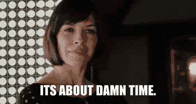 a woman is standing in front of a wall and saying `` it 's about damn time . ''