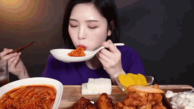 a woman is sitting at a table eating food with chopsticks and a spoon .