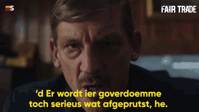 a man with a mustache is talking with the words fair trade in the background