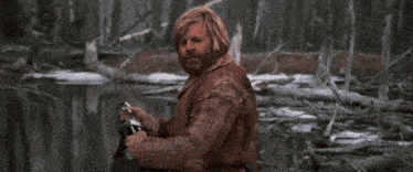 a man with a beard is standing in the woods holding a bottle