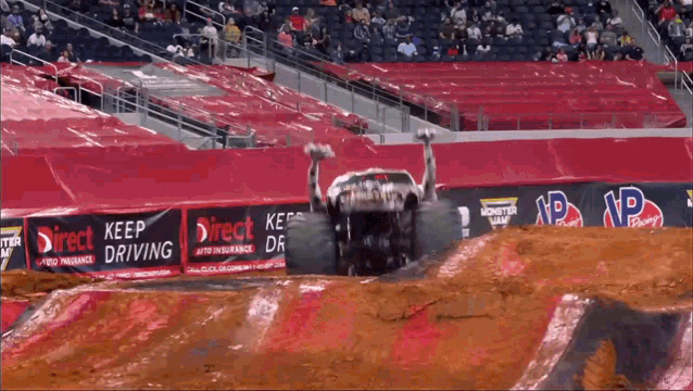 a monster truck jumps over a dirt track in front of a sign that says " keep driving "