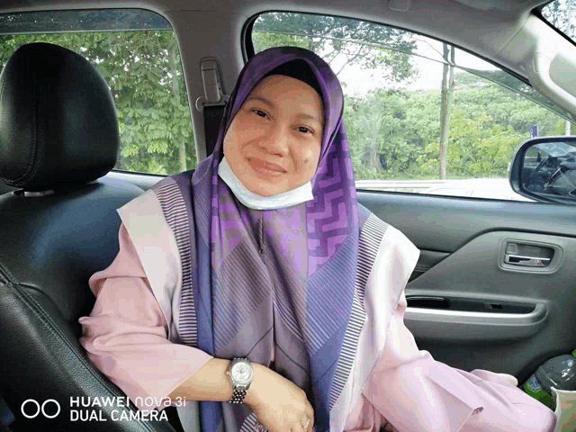 a woman wearing a purple scarf sits in the back seat of a car with a huawei nova 3i dual camera