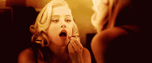 a woman is looking at herself in the mirror while applying lipstick .