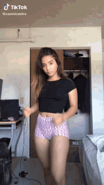 a woman in a black top and pink shorts is dancing in a bedroom .
