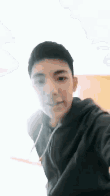 a young man is taking a selfie with his phone while wearing a black hoodie .