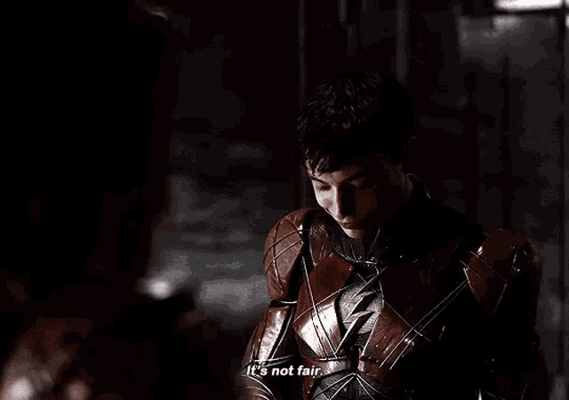 a man in a superhero costume is talking to another man in a dark room .