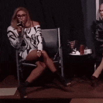 a woman is sitting in a chair with her legs crossed and talking into a microphone