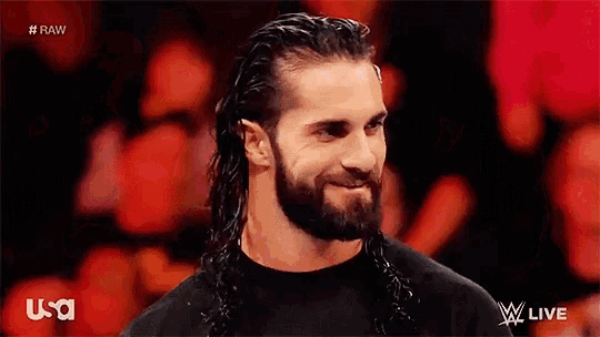 a man with long hair and a beard is smiling and wearing a black shirt that says usa