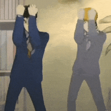 two men in suits are standing next to each other in a room holding their heads in the air .